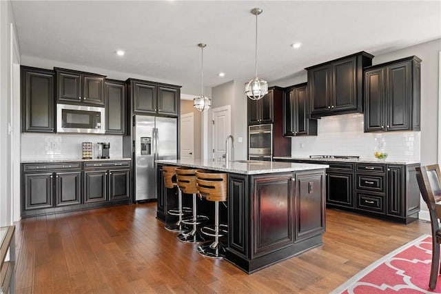 1735 Stevensan Dr, Franklin Park, PA 15143 - kitchen with appliances with stainless steel finishes, tasteful backsplash, hanging light fixtures, dark wood-type flooring, and an island with sink