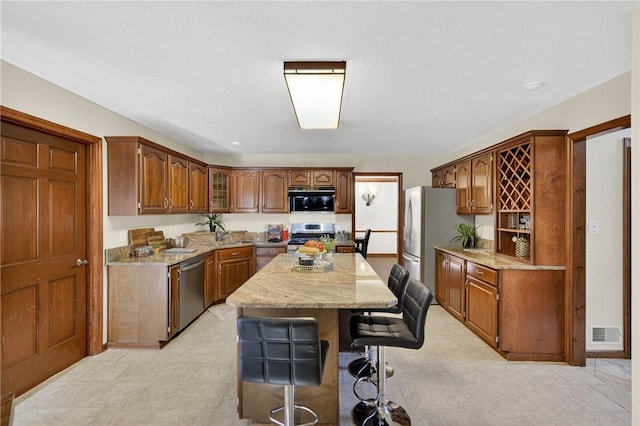 2455 Dogwood Dr, Franklin Park, PA 15090 - kitchen with appliances with stainless steel finishes, a kitchen island, light stone countertops, a breakfast bar, and brown cabinetry