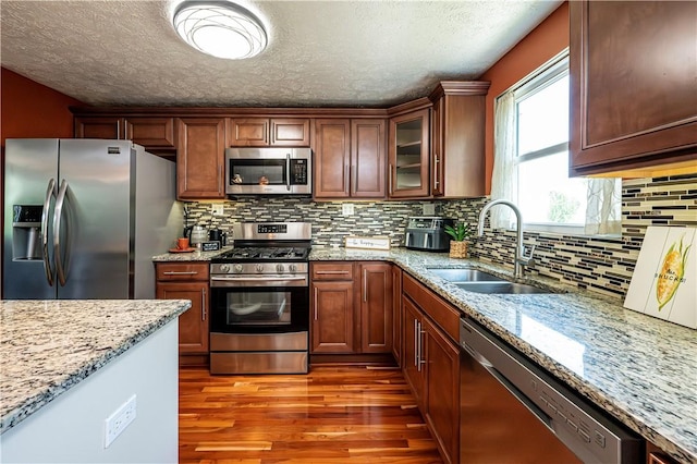 221 Wheatfield Dr, Hempfield Twp, PA 15601 - kitchen featuring appliances with stainless steel finishes, wood finished floors, a textured ceiling, light stone counters, and glass insert cabinets