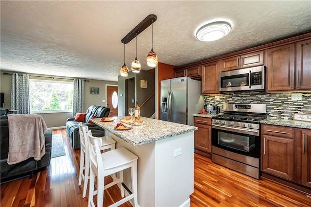 221 Wheatfield Dr, Hempfield Twp, PA 15601 - kitchen with appliances with stainless steel finishes, open floor plan, hardwood / wood-style floors, a textured ceiling, and a breakfast bar area