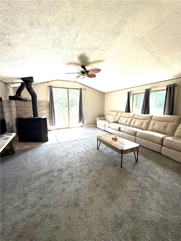 6028 Davidson Rd, Jamestown, PA 16134 - carpeted living area featuring a wood stove, ceiling fan, lofted ceiling, and a textured ceiling
