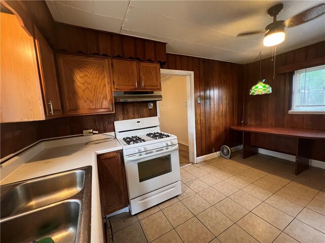 2220 Cronemeyer St, Mckeesport, PA 15132 - kitchen featuring white gas range, under cabinet range hood, light countertops, wooden walls, and light tile patterned floors