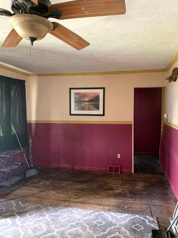 232 Fairview Ave, Masontown, PA 15461 - empty room featuring a textured ceiling, a wainscoted wall, wood finished floors, ornamental molding, and a ceiling fan