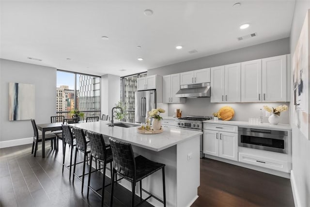 350 Oliver Ave Unit 1301/1401, Downtown Pgh, PA 15222 - kitchen with under cabinet range hood, stainless steel appliances, a center island with sink, white cabinetry, and recessed lighting