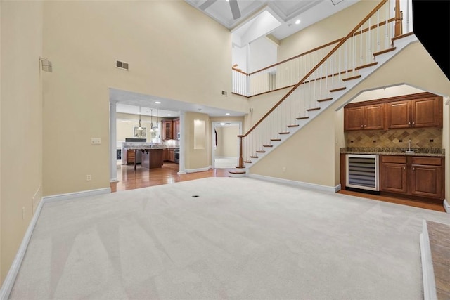 402 Providence Ct, Adams Twp, PA 16059 - unfurnished living room with wine cooler, light carpet, bar with sink, a towering ceiling, and stairs