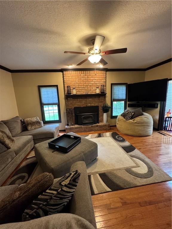 91 Celtic Ash Ct, Cranberry Twp, PA 16066 - living room featuring wood finished floors, a brick fireplace, a ceiling fan, a textured ceiling, and crown molding
