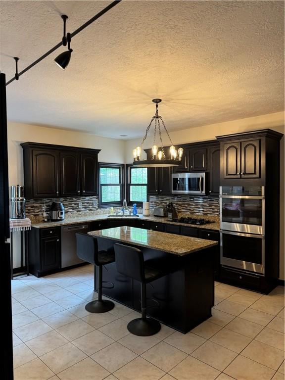 91 Celtic Ash Ct, Cranberry Twp, PA 16066 - kitchen featuring stainless steel appliances, backsplash, a textured ceiling, a kitchen bar, and light tile patterned flooring