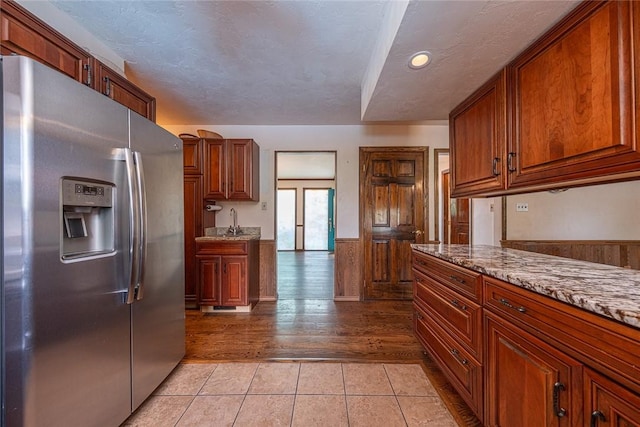 315 Pennsylvania Ave, Plum Boro, PA 15147 - kitchen with stainless steel fridge with ice dispenser, a wainscoted wall, light tile patterned floors, brown cabinetry, and light stone countertops