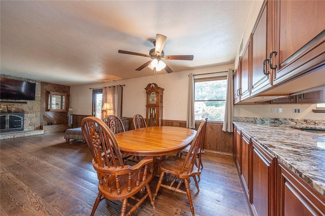 315 Pennsylvania Ave, Plum Boro, PA 15147 - dining area featuring dark wood finished floors, a wainscoted wall, a stone fireplace, wooden walls, and ceiling fan