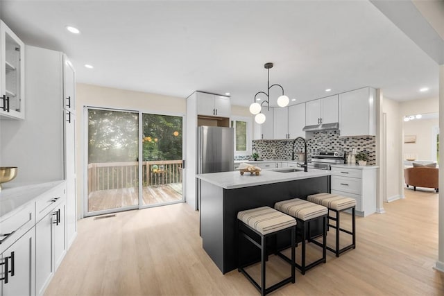 1014 Olga St, Ambridge, PA 15003 - kitchen with under cabinet range hood, stainless steel appliances, light wood-style flooring, decorative backsplash, and white cabinets
