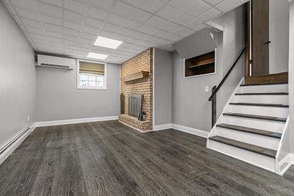 408 Circle Dr, Franklin Twp, PA 16117 - unfurnished living room with a wall mounted AC, wood finished floors, a brick fireplace, a baseboard heating unit, and stairway