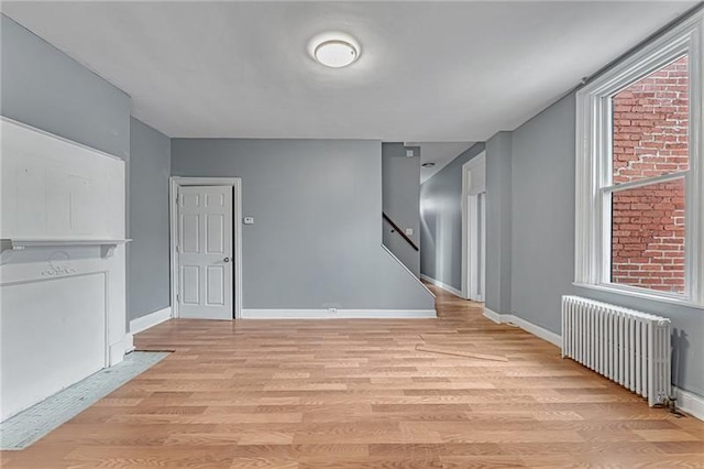 375 Main St, Lawrenceville, PA 15201 - unfurnished living room with radiator heating unit, light wood-style floors, and stairway