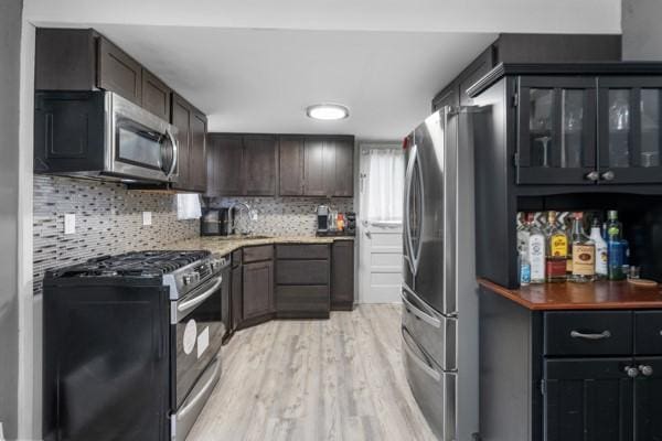 147 Rodilin Dr, Penn Hills, PA 15235 - kitchen featuring appliances with stainless steel finishes, light wood finished floors, tasteful backsplash, glass insert cabinets, and dark brown cabinets