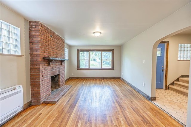 9502 Frankstown, Penn Hills, PA 15235 - unfurnished living room featuring light wood-style floors, arched walkways, a brick fireplace, heating unit, and stairway