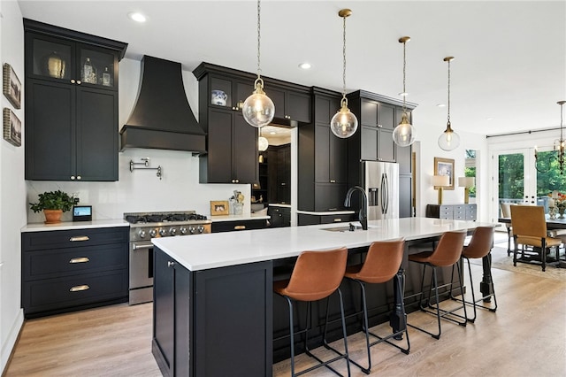 3901 Bakerstown Rd, Richland, PA 15044 - kitchen with custom exhaust hood, appliances with stainless steel finishes, a kitchen island with sink, light countertops, and light wood finished floors