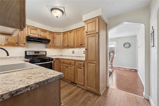 1417 Riverview Dr, Verona, PA 15147 - kitchen featuring under cabinet range hood, stainless steel range with gas stovetop, arched walkways, wood finished floors, and light countertops