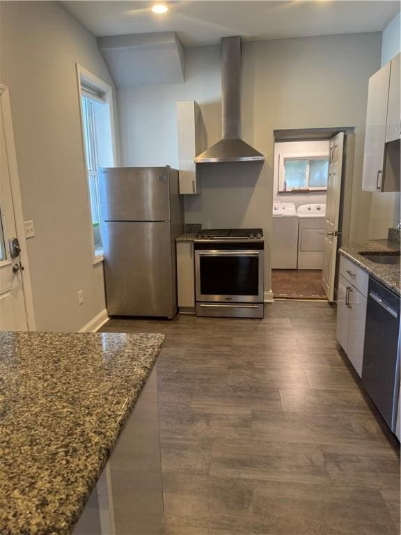 2411 Sarah St, South Side, PA 15203 - kitchen featuring stainless steel appliances, wall chimney range hood, washer and clothes dryer, dark stone countertops, and dark wood-style floors