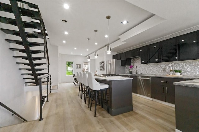 2613 Stella St, South Side, PA 15203 - kitchen with stainless steel appliances, light wood-style floors, decorative backsplash, a center island, and a kitchen breakfast bar