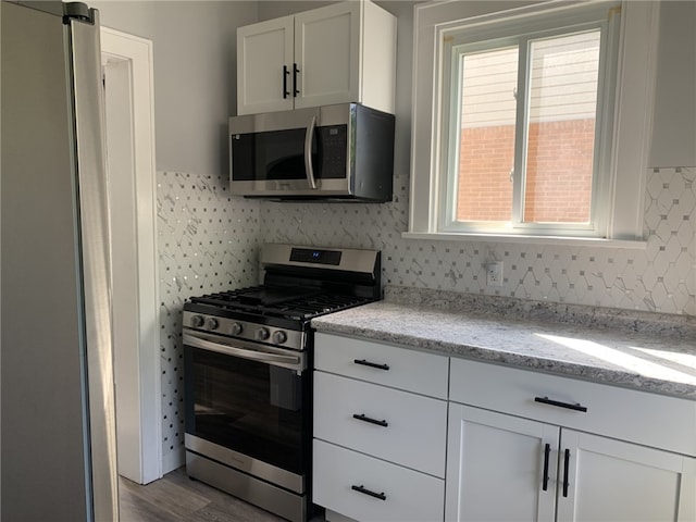 1101 State Route 356, Allegheny Twp, PA 15656 - kitchen featuring stainless steel appliances, backsplash, white cabinets, light stone counters, and wood finished floors