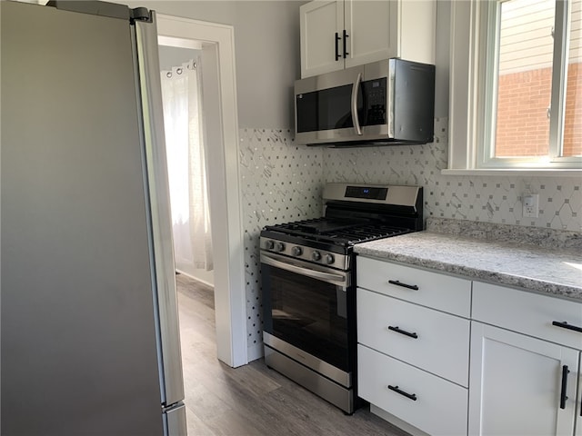 1101 State Route 356, Allegheny Twp, PA 15656 - kitchen with appliances with stainless steel finishes, wood finished floors, tasteful backsplash, white cabinetry, and light stone counters