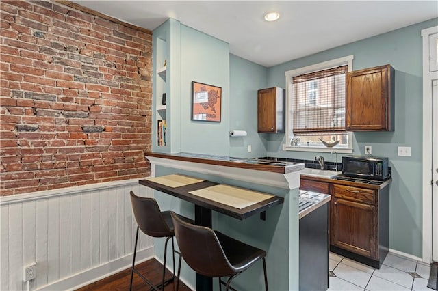175-177 43rd 1/2 St, Lawrenceville, PA 15201 - kitchen with brick wall, black microwave, a kitchen breakfast bar, light tile patterned floors, and brown cabinets