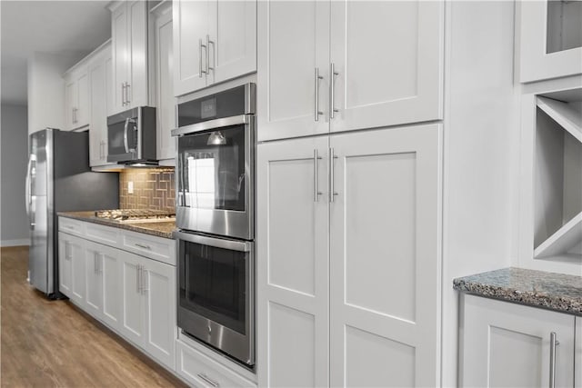 152 Cole Dr, Robinson Twp, PA 15136 - kitchen with appliances with stainless steel finishes, tasteful backsplash, dark stone countertops, wood finished floors, and white cabinetry