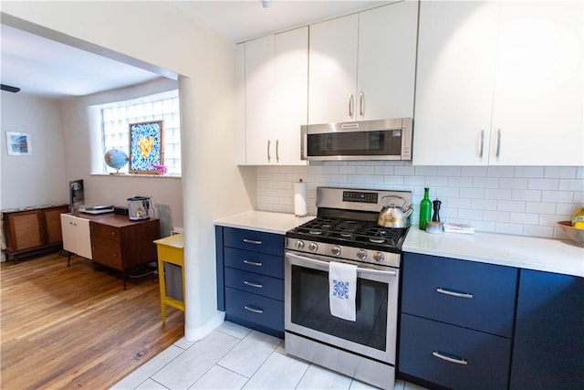 5553 Pocusset St, Squirrel Hill, PA 15217 - kitchen featuring appliances with stainless steel finishes, blue cabinets, light countertops, decorative backsplash, and white cabinetry