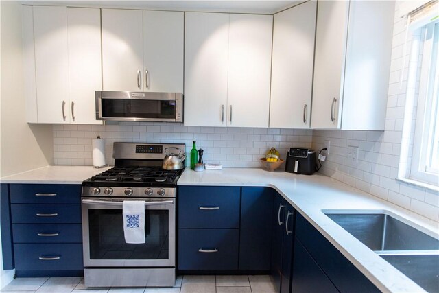 5553 Pocusset St, Squirrel Hill, PA 15217 - kitchen with stainless steel appliances, blue cabinetry, decorative backsplash, and white cabinetry