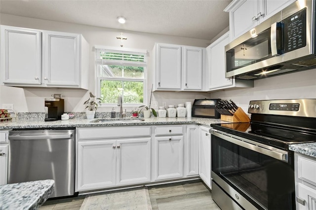 329 Nelson Dr, Monroeville, PA 15146 - kitchen featuring stainless steel appliances, white cabinets, light wood-style flooring, light stone countertops, and a textured ceiling
