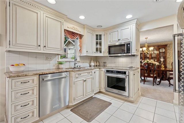 511 Brunswick Dr, Hempfield Twp, PA 15601 - kitchen featuring appliances with stainless steel finishes, cream cabinetry, a chandelier, light stone countertops, and light carpet