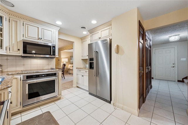 511 Brunswick Dr, Hempfield Twp, PA 15601 - kitchen with stainless steel appliances, cream cabinets, light tile patterned floors, light stone countertops, and decorative backsplash