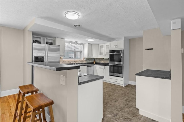 109 Raleigh Ct, Ross Twp, PA 15237 - kitchen featuring appliances with stainless steel finishes, a kitchen breakfast bar, dark countertops, a textured ceiling, and glass insert cabinets