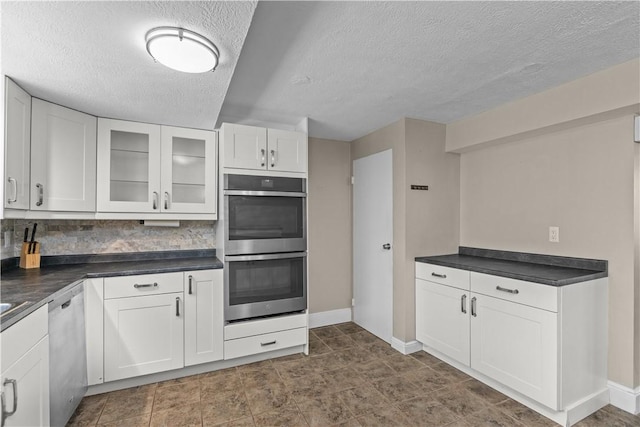 109 Raleigh Ct, Ross Twp, PA 15237 - kitchen with stainless steel appliances, a textured ceiling, dark countertops, white cabinetry, and glass insert cabinets
