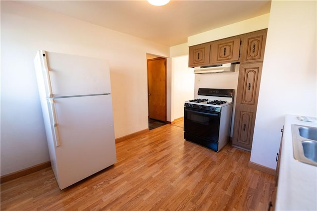 1819 Sundeman St, Troy Hill, PA 15212 - kitchen featuring freestanding refrigerator, gas range, under cabinet range hood, light wood-style floors, and brown cabinetry