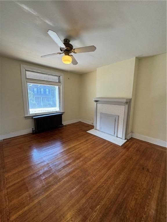 207 N Sprague Ave, Bellevue, PA 15202 - unfurnished living room with radiator heating unit, wood finished floors, a fireplace with flush hearth, and ceiling fan