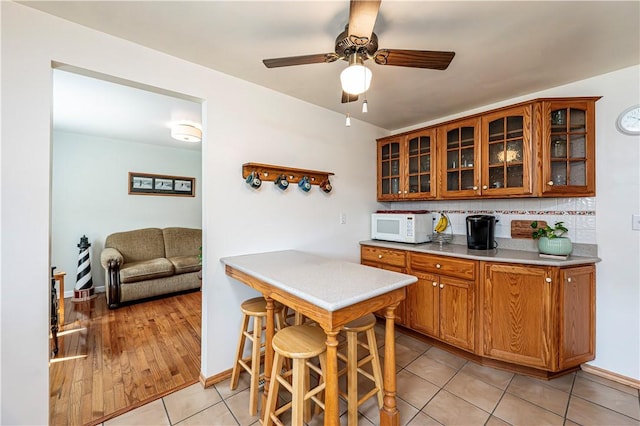 209 Farmbrook Dr, Hempfield Twp, PA 15601 - kitchen with white microwave, brown cabinets, backsplash, glass insert cabinets, and light tile patterned floors