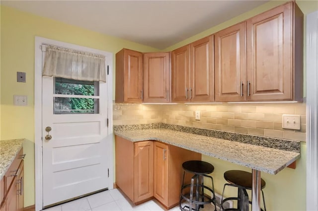 7034 Penn Ave, Point Breeze, PA 15208 - kitchen featuring light stone countertops, backsplash, a breakfast bar, and light tile patterned flooring