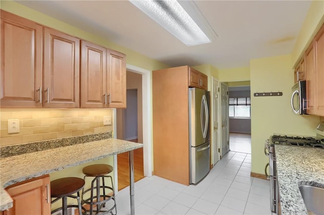 7034 Penn Ave, Point Breeze, PA 15208 - kitchen with appliances with stainless steel finishes, tasteful backsplash, a breakfast bar area, light tile patterned flooring, and light stone counters