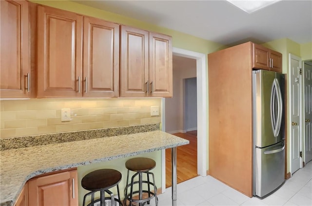 7034 Penn Ave, Point Breeze, PA 15208 - kitchen featuring freestanding refrigerator, decorative backsplash, a breakfast bar, light stone countertops, and light tile patterned flooring