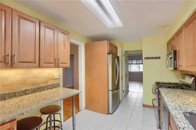 7034 Penn Ave, Point Breeze, PA 15208 - kitchen with appliances with stainless steel finishes, decorative backsplash, light stone counters, a breakfast bar area, and light tile patterned flooring