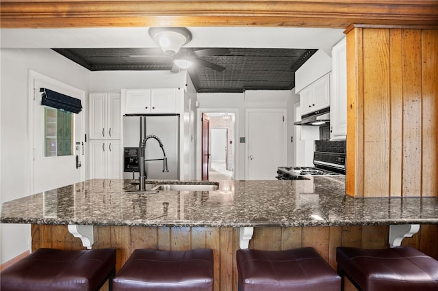 1302 Mount Royal Blvd, Shaler, PA 15223 - kitchen with range with gas stovetop, under cabinet range hood, stainless steel fridge, dark stone countertops, and a kitchen bar