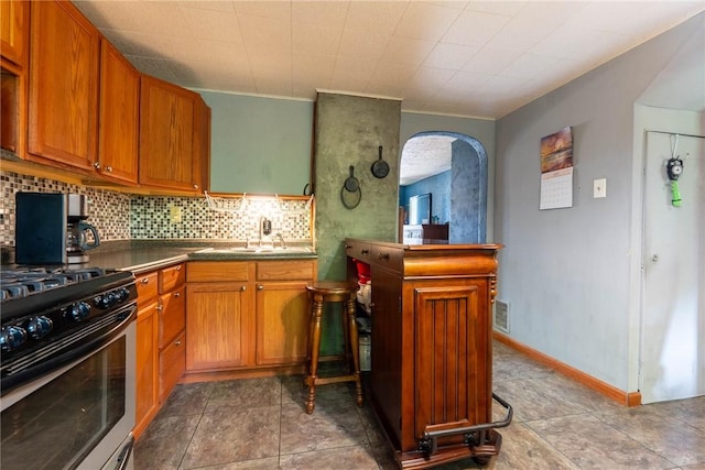 309 Francis Ave, Monongahela, PA 15063 - kitchen featuring gas range oven, backsplash, brown cabinetry, dark countertops, and arched walkways
