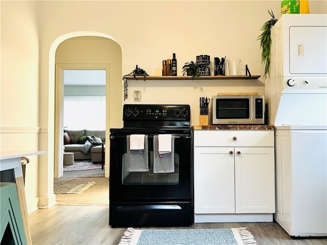 657 Grove St, City Of Greensburg, PA 15601 - kitchen featuring black electric range, stainless steel microwave, stacked washing machine and dryer, light wood-style flooring, and white cabinetry