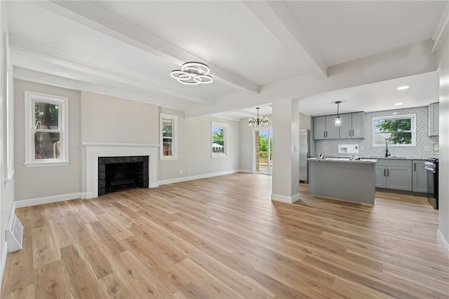327 Charles Ave, New Kensington, PA 15068 - unfurnished living room featuring a chandelier, light wood-type flooring, a fireplace, and beam ceiling