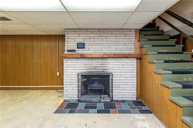 127 Mount Odin Dr, Hempfield Twp, PA 15601 - unfurnished living room featuring a paneled ceiling, a brick fireplace, wood walls, and stairs