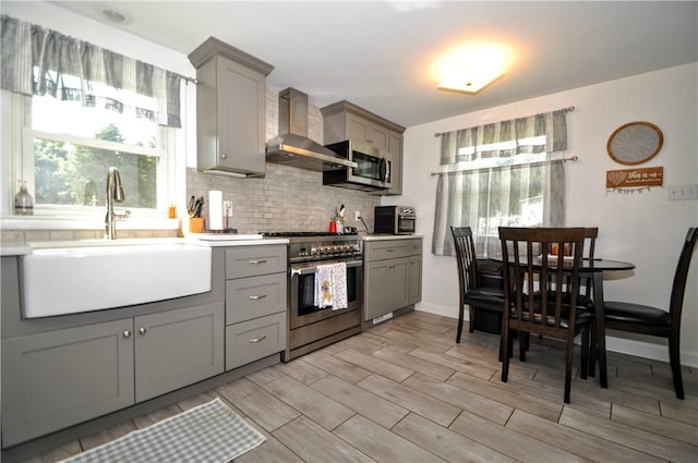 111 Wood St, Rostraver, PA 15089 - kitchen with gray cabinets, wall chimney range hood, appliances with stainless steel finishes, decorative backsplash, and healthy amount of natural light