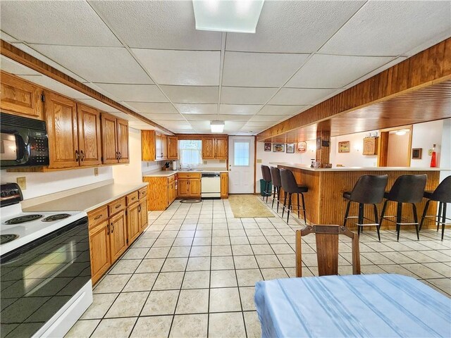1031 Gameland Rd, Donegal, PA 16025 - kitchen with white appliances, a paneled ceiling, light tile patterned floors, a kitchen bar, and brown cabinetry