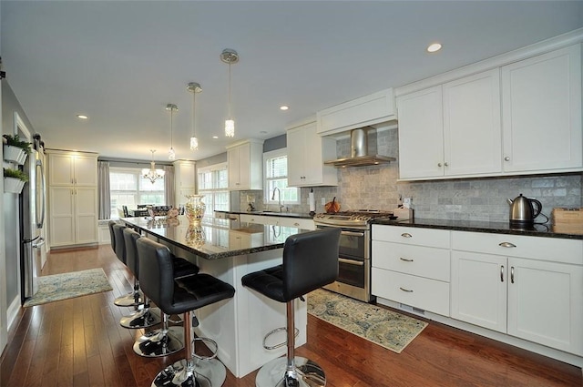 79 W Manilla Ave, Green Tree, PA 15220 - kitchen featuring appliances with stainless steel finishes, wall chimney exhaust hood, decorative backsplash, white cabinetry, and a kitchen island