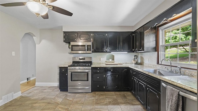 900 N Whitmore Rd, North Huntingdon, PA 15642 - kitchen with appliances with stainless steel finishes, arched walkways, a ceiling fan, decorative backsplash, and dark cabinetry