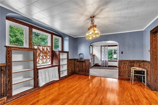 200 38th St, Beaver Falls, PA 15010 - unfurnished living room featuring arched walkways, plenty of natural light, a wainscoted wall, wood-type flooring, and crown molding